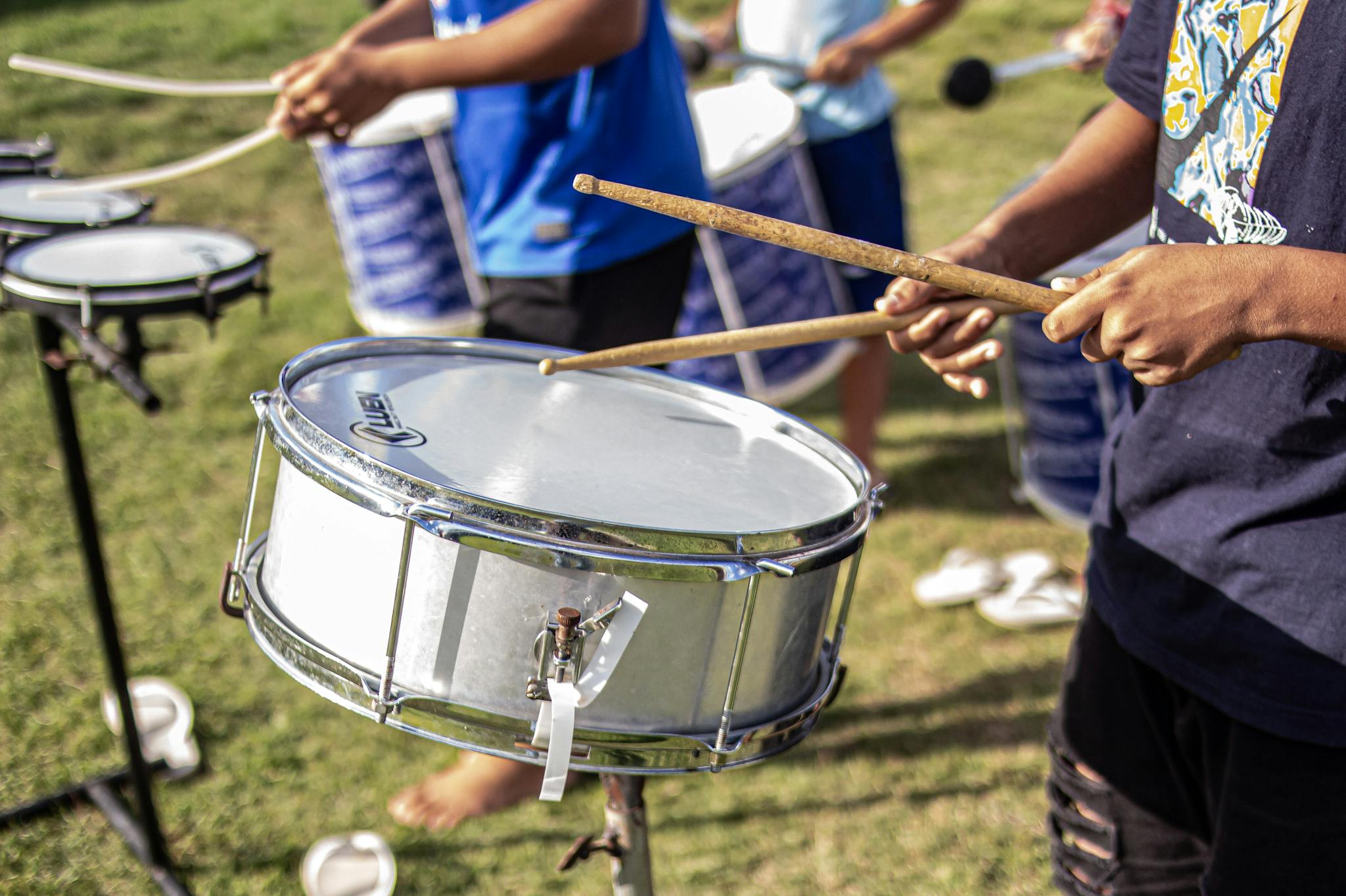 Group of drummers performing outdoors, engaging in lively percussion ensemble on a sunny day.